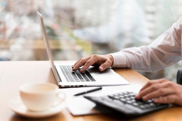 A businessman typing on a laptop and also using a calculator