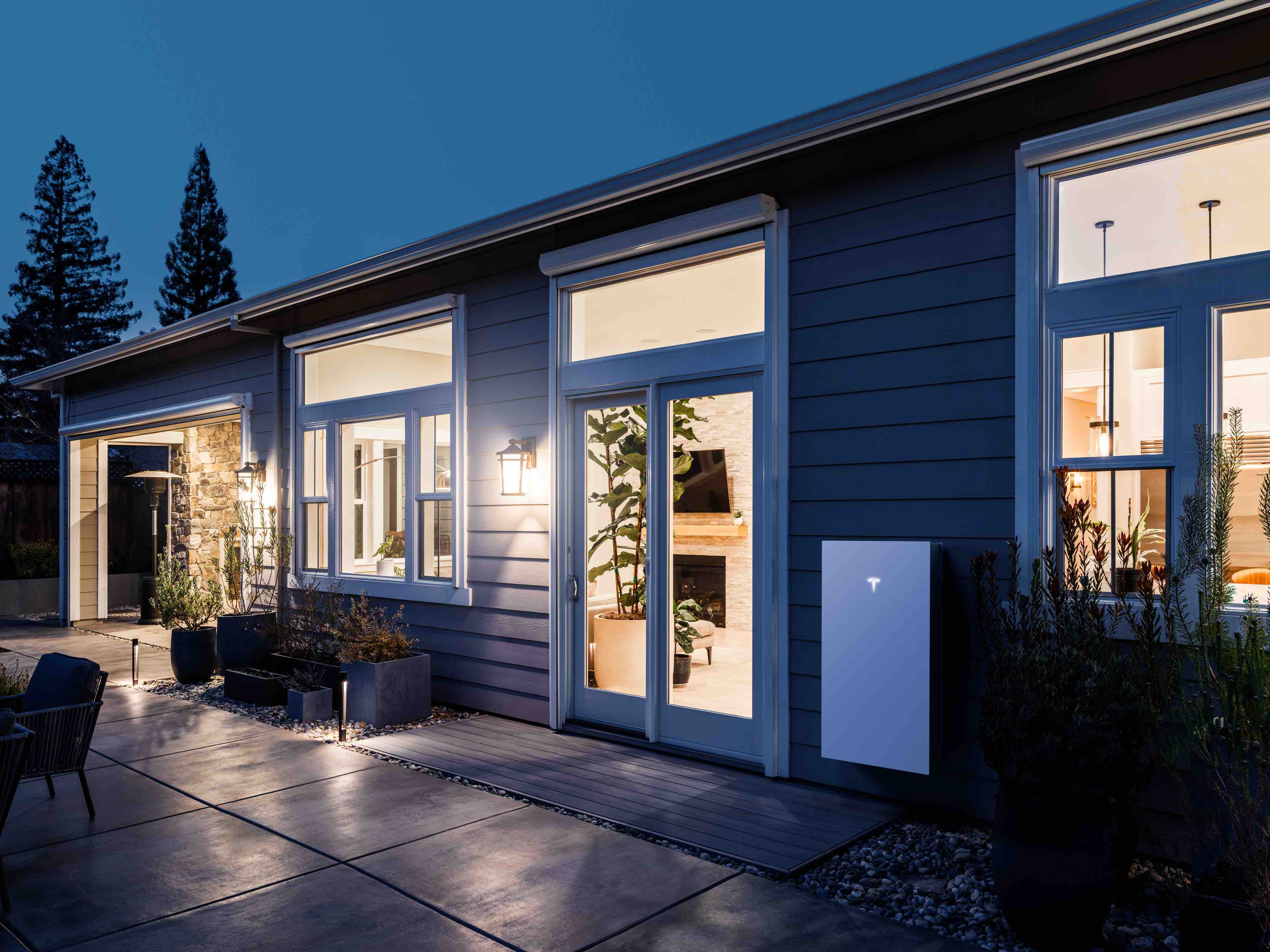 A photo of a Tesla Powerwall battery installed on the exterior wall of home at night